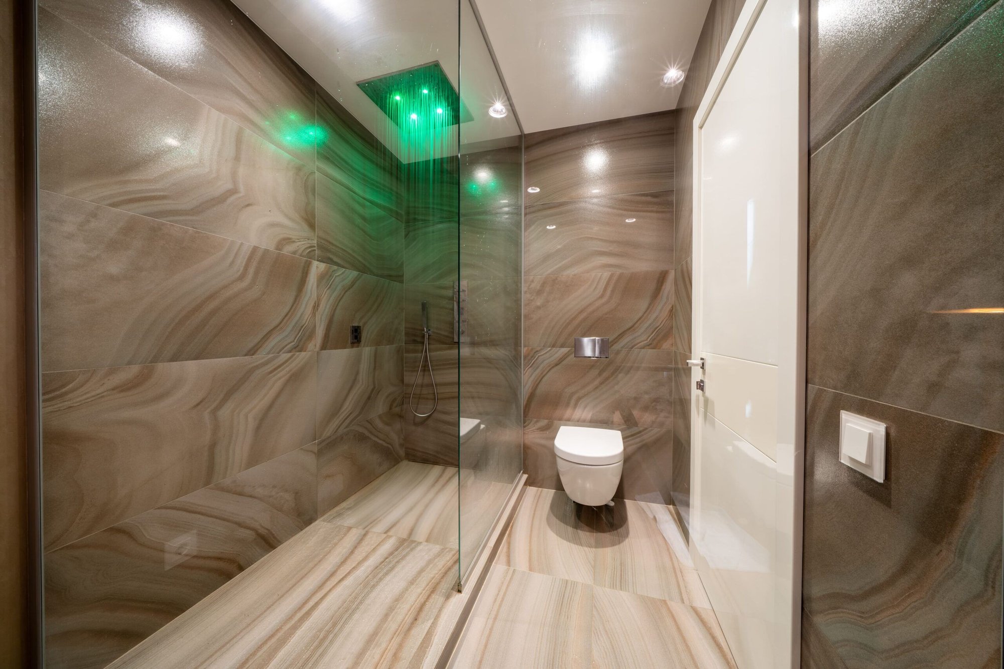 baño en tonos marrones y luces integradas en el techo y ducha con iluminacion