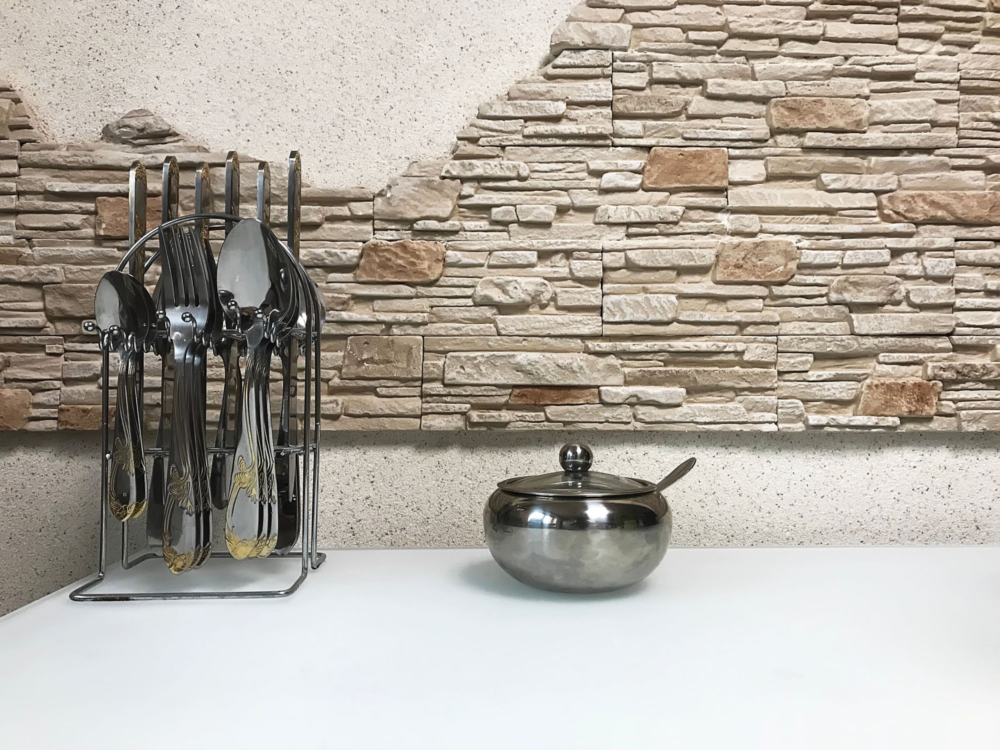 detalle de mesa de cocina con cubiertos y una pared de piedra artificial al fondo