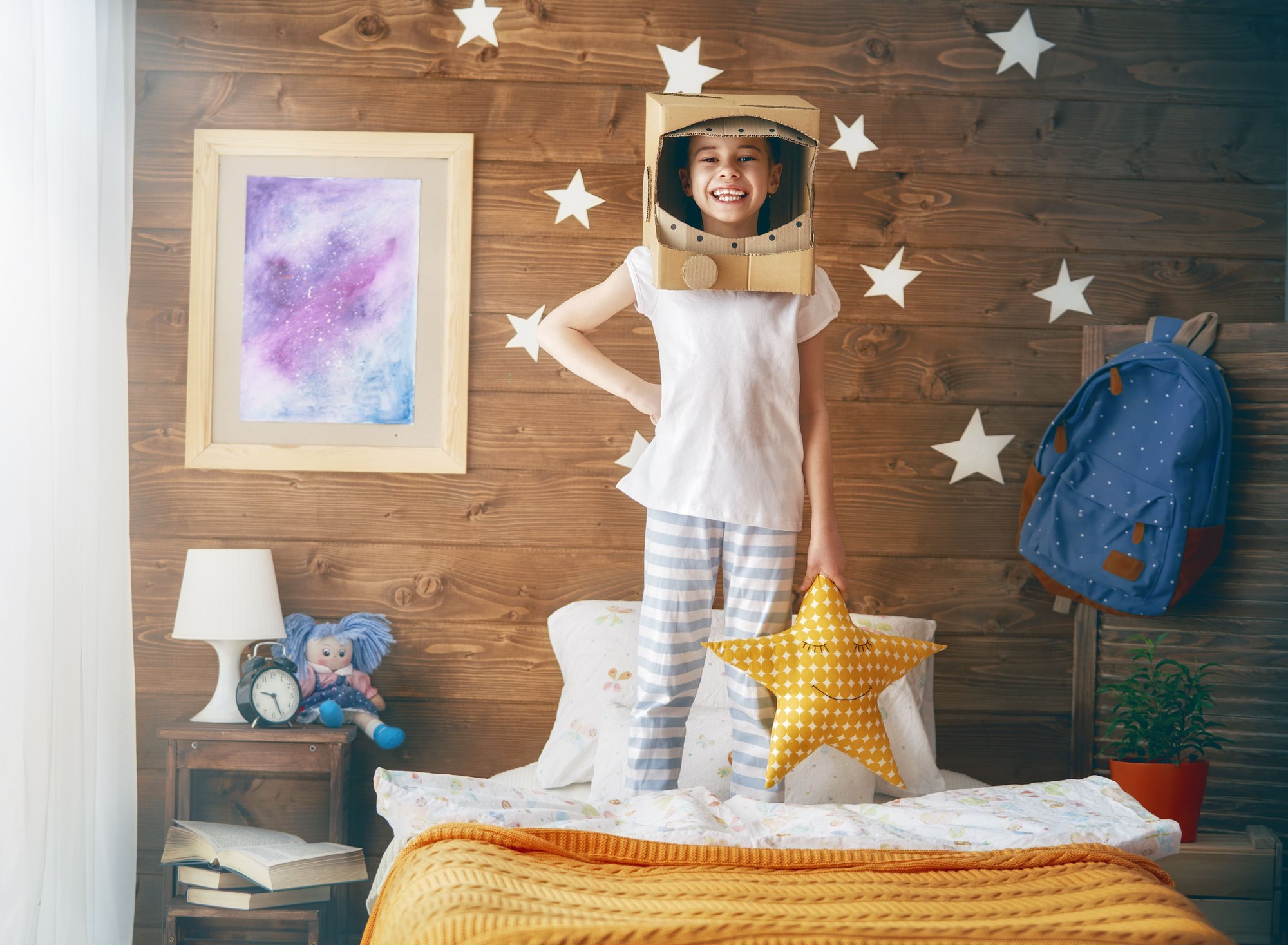 niña pequeña en su habitacion con casco de astronauta de jueguete y estrellas de luces
